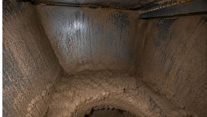 Inside view of an industrial dust collector hopper showing severe dust bridging caused by moisture and condensation, restricting material discharge.
