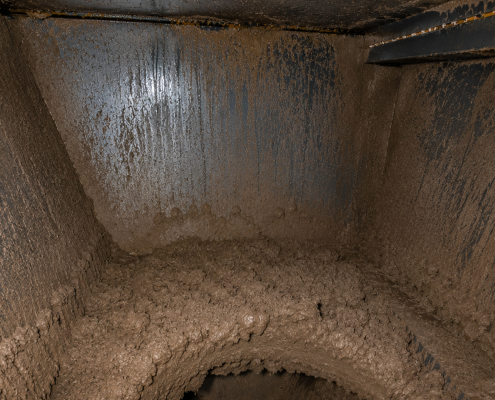 Inside view of an industrial dust collector hopper showing severe dust bridging caused by moisture and condensation, restricting material discharge.