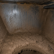 Inside view of an industrial dust collector hopper showing severe dust bridging caused by moisture and condensation, restricting material discharge.