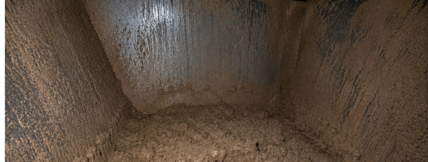 Inside view of an industrial dust collector hopper showing severe dust bridging caused by moisture and condensation, restricting material discharge.