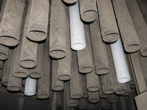 Inside an industrial baghouse showing mostly dirty filter bags with three new replacement filter bags installed among them during maintenance.